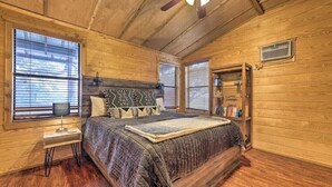 A cozy wooden bedroom with a large bed, a nightstand, a bookshelf, and a ceiling fan.
