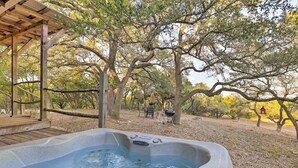 A hot tub in a wooded area with a wooden pergola and a picnic table in the background.