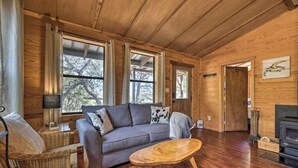 A cozy living room with a wooden ceiling, a gray sofa, a wicker chair, and a wooden coffee table.
