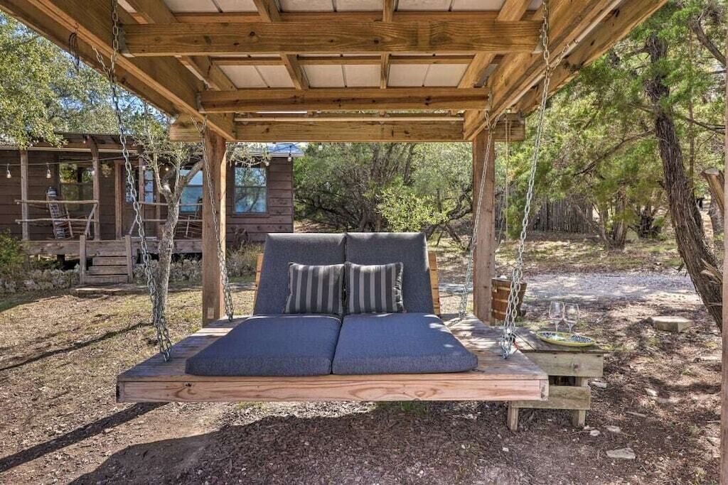 Un lit-balançoire en bois, doté de coussins et accompagné d’une petite table sur laquelle se trouvent un verre et une assiette.
