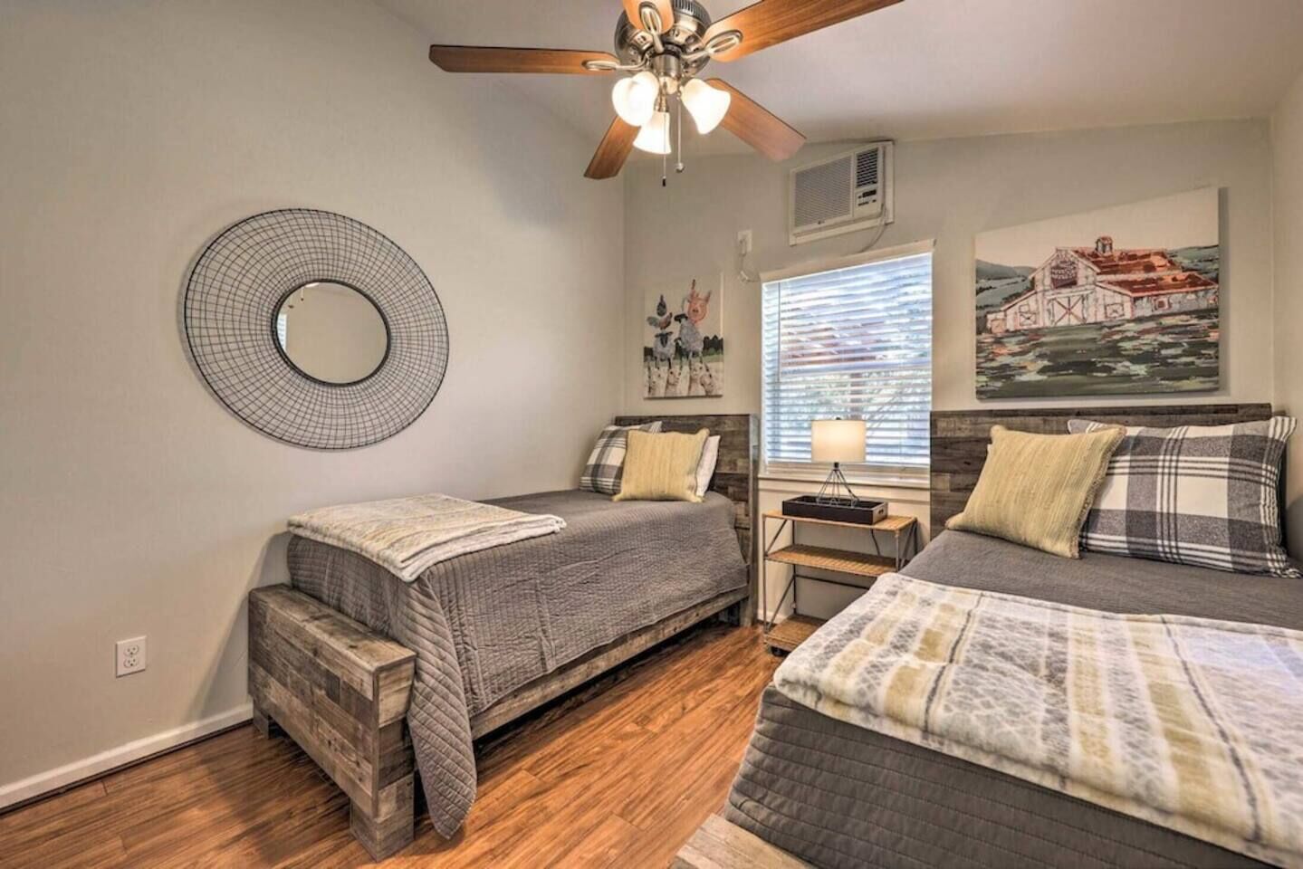 A bedroom with two beds, a ceiling fan, a wall-mounted mirror, and a window with blinds.