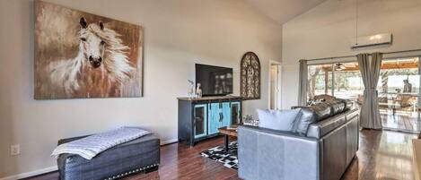 A spacious living room with a large painting, a sofa, a bench, and a TV on a cabinet.