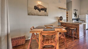 A dining area with a wooden table and chairs, a kitchen in the background, and a buffalo painting on the wall. - Las Estrellas Lots of privacy with stunning views, 2 decks, private hot tub! (Wimberley)