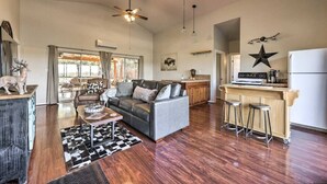 A spacious living area with a grey sofa, wooden flooring, and a ceiling fan. - Las Estrellas Lots of privacy with stunning views, 2 decks, private hot tub! (Wimberley)