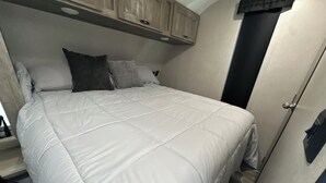 Een net opgemaakt bed met een witte dekbedovertrek, een houten hoofdbord en een deur aan de rechterkant.