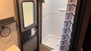 Een kleine badkamer met een douche, een raam en een handdoekhouder.