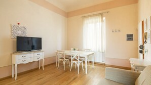 Un salon comprenant un téléviseur, une table à manger, des chaises, un canapé et une fenêtre avec des rideaux.