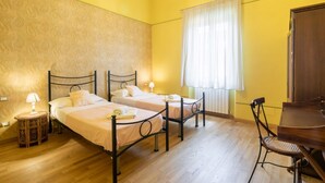 Une chambre avec deux lits, une table en bois, une chaise, une lampe et une fenêtre avec des rideaux.