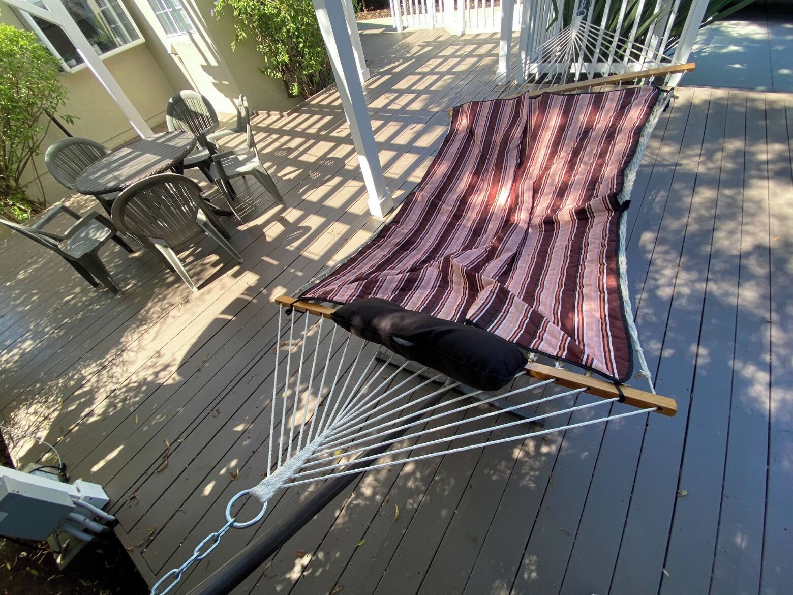 Eine Hängematte auf einer Holzterrasse mit einer gestreiften Decke und einem schwarzen Kissen.
