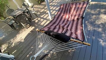 Eine Hängematte auf einer Holzterrasse mit einer gestreiften Decke und einem schwarzen Kissen.