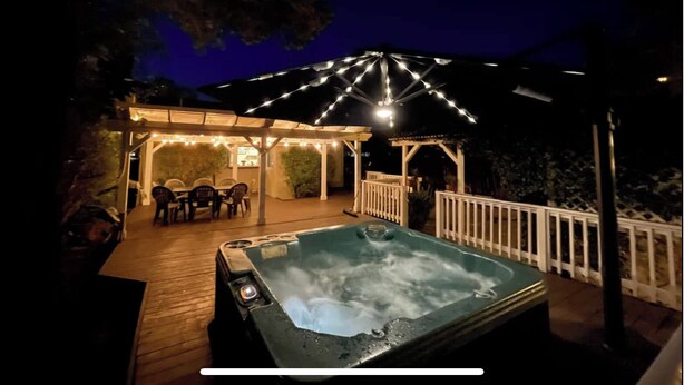 Een hottub op een houten terras met een overdekte patio en sfeerverlichting.