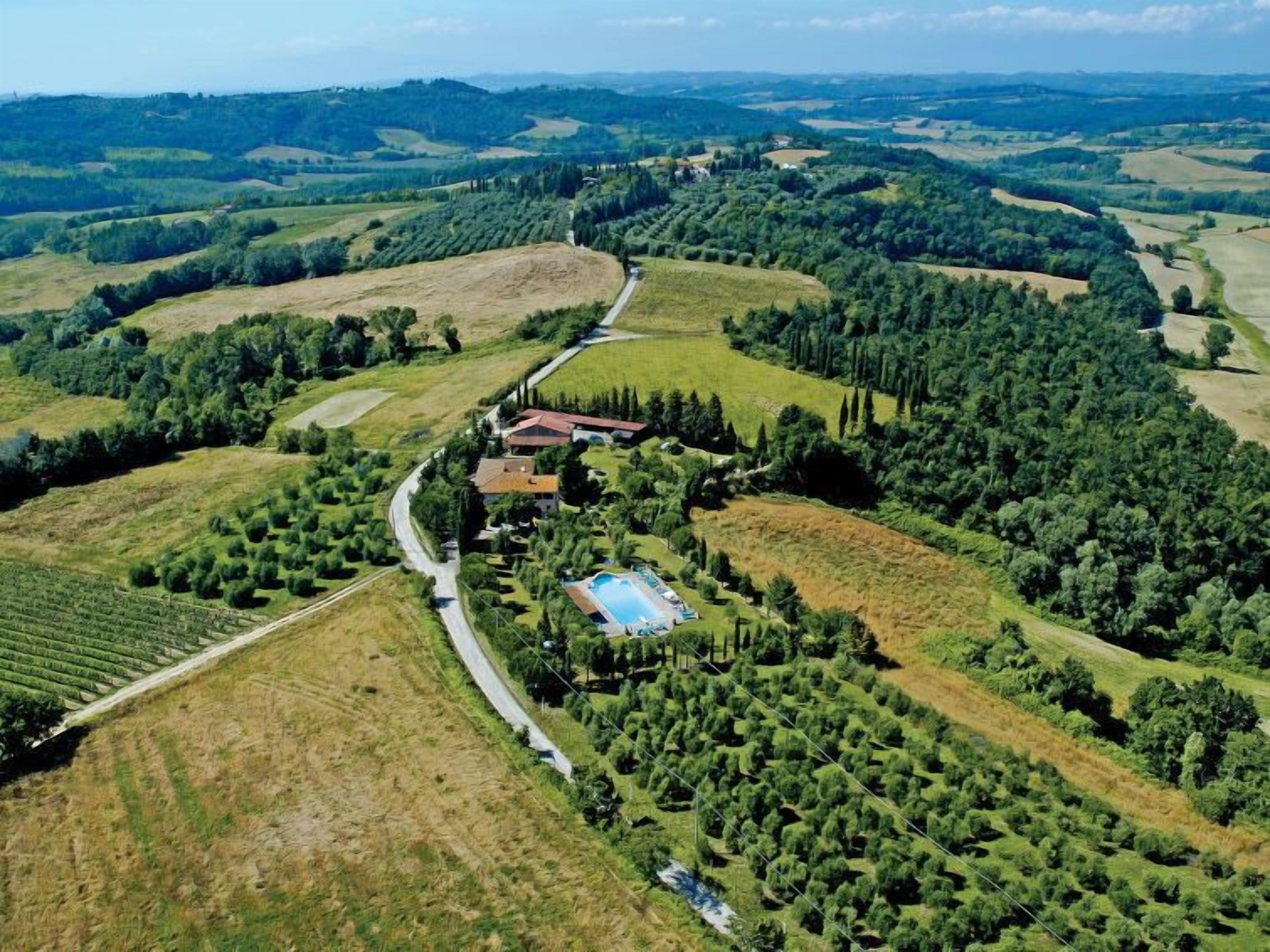 An aerial view of a rural property with a winding road, a swimming pool, and surrounding fields.