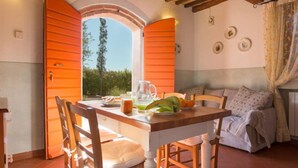 A dining area with a table set for two, a window with open shutters, and a view of greenery outside. - Apartment Mimosa by Interhome (Peccioli)