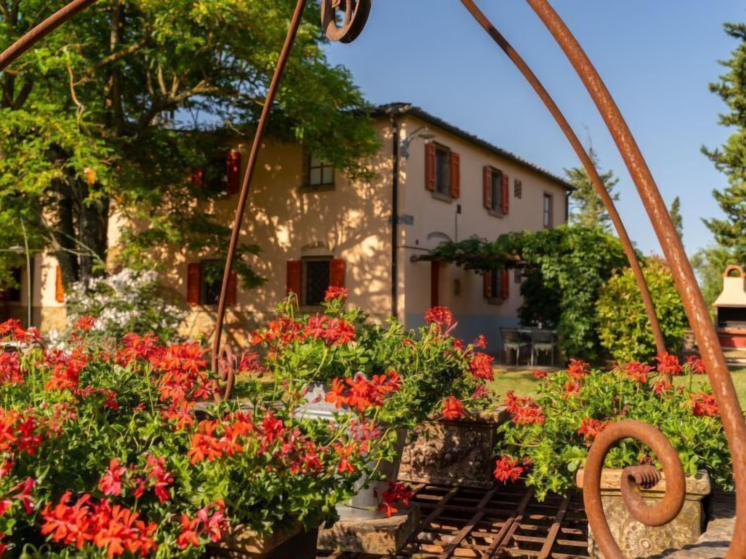 Un bâtiment rustique avec un jardin à l’avant, agrémenté de fleurs rouges et doté d’une structure métallique.