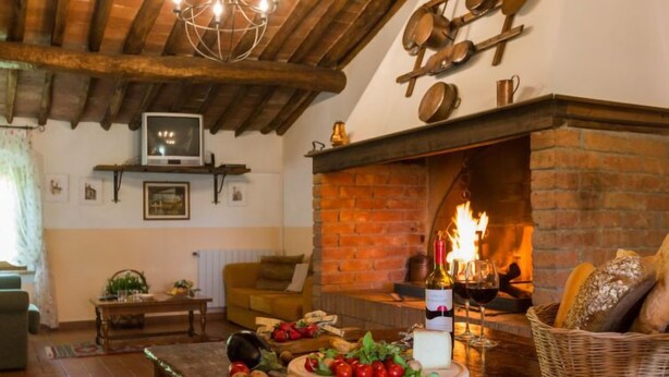 A cozy living room with a fireplace, wooden beams, a television, and a table with food and drinks. - Apartment Mimosa by Interhome (Peccioli)