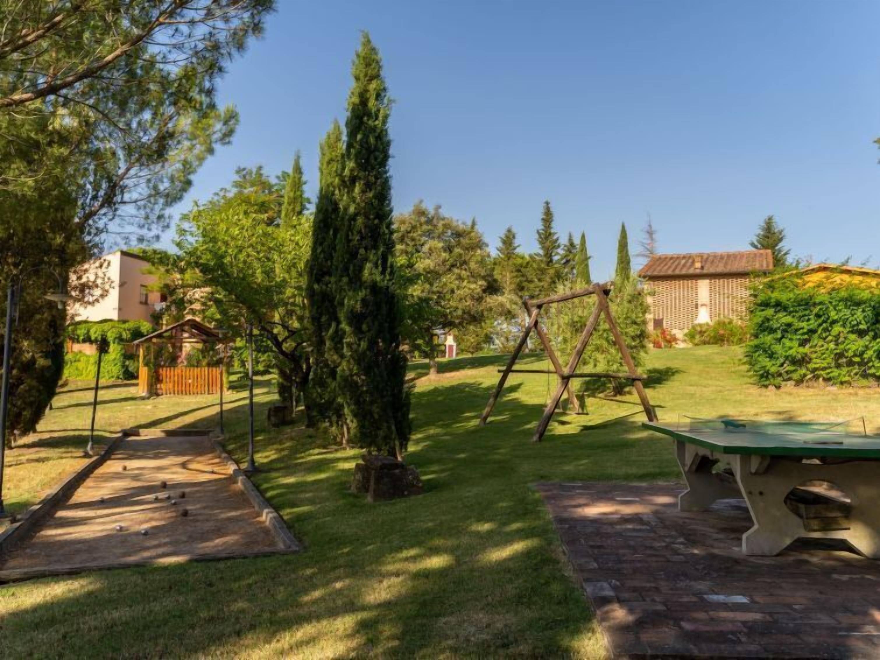 Un jardin avec une balançoire en bois, un terrain de pétanque et une table de pique-nique.