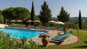 A pool area with lounge chairs and umbrellas, surrounded by greenery and trees. - Apartment Mimosa by Interhome (Peccioli)