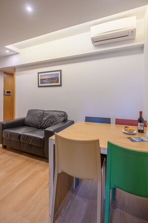 A modern room with a wooden dining table, a leather sofa, and a wall-mounted air conditioner.