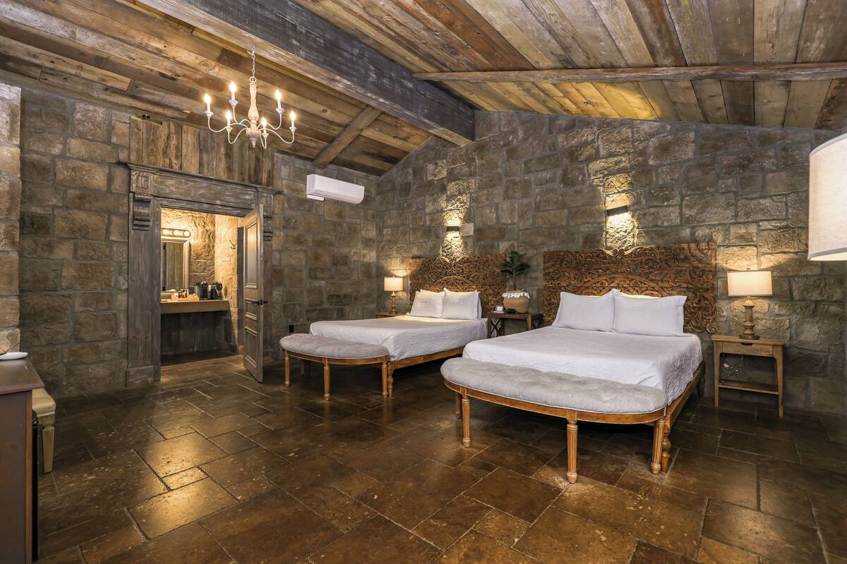 A rustic room with two beds, stone walls, and a wooden ceiling.