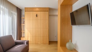 A modern living room with a sofa, wooden wardrobe, and a flat-screen TV on a wooden shelf. - Northern Star - Studio 1.1 Porto (in the city center) (Porto)