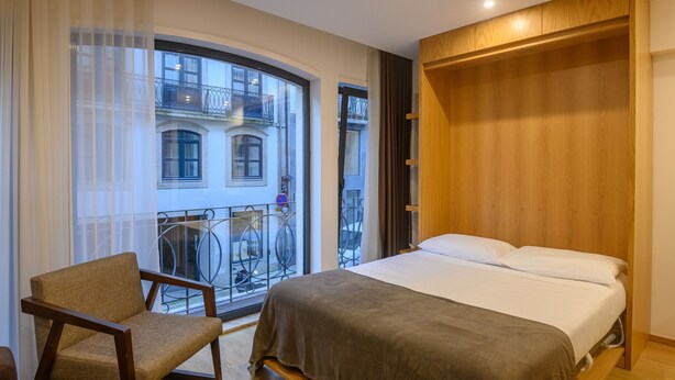 A bedroom with a large bed, a chair, a wooden wardrobe, and a balcony with a railing. - Northern Star - Studio 1.1 Porto (in the city center) (Porto)