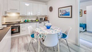 A modern kitchen with white cabinets, a microwave, and a sink. There is a dining table with chairs and a blue bowl. - Apartment Moracea near the beach (Njivice)