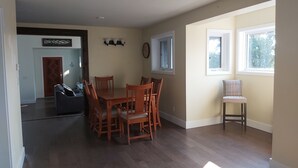 A spacious dining area with a wooden table and chairs, a small seating area by a window, and a hallway leading to a door.