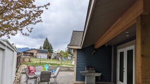A patio with outdoor seating, a grill, and a view of a residential area with houses and mountains in the background.