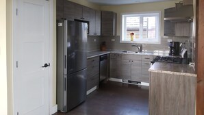 A modern kitchen with a stainless steel refrigerator, wooden cabinets, a built-in oven, and a window providing natural light.