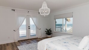 A bedroom with a large bed, a view of the beach, and a white chandelier.
