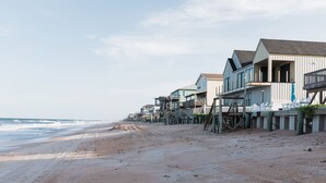 A beachfront property with multiple houses elevated on stilts, a sandy beach, and the ocean in the background.