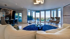 A spacious living room with a round coffee table, white sofas, and a large TV.