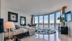 A modern bedroom with a bed, a TV, and a large window with a view of the landscape.