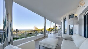 A modern balcony with white furniture, a glass balustrade, and a view of the sea.