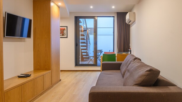 Ein modernes Wohnzimmer mit einer Couch, einem Fernseher, einer Holzkommode und einer Glastür, die auf einen Balkon führt.