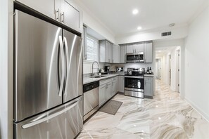 A modern kitchen with stainless steel appliances, a marble floor, and a hallway leading to other rooms. - Modern Upscale 5BR/5BA (4 en suite) Home near Superdome and French Quarter (New Orleans)