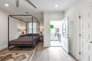 A bedroom with a four-poster bed, bedside lamps, a view through an open door to a balcony, and a wooden floor. - Modern Upscale 5BR/5BA (4 en suite) Home near Superdome and French Quarter (New Orleans)