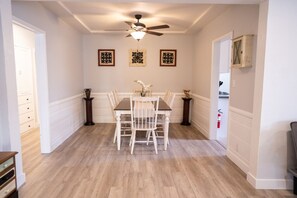 Un espace repas comprenant une table et des chaises en bois, un ventilateur de plafond et des œuvres d’art accrochées au mur.