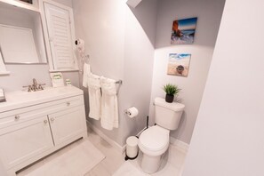 Une salle de bain avec un meuble-lavabo blanc, des toilettes et une petite plante en pot.
