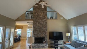 A spacious living area with a stone fireplace, a ceiling fan, a flat-screen TV, and a balcony. - The View on Weiss Lake (cedar bluff)