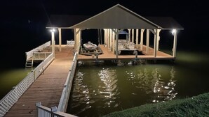 A docked boat with a covered seating area and a small table, surrounded by water. - The View on Weiss Lake (cedar bluff)