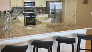 A kitchen with white cabinets, a granite countertop, stainless steel appliances, and a bar area with stools. - The View on Weiss Lake (cedar bluff)