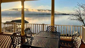 A covered outdoor area with a table and chairs, overlooking a body of water and a distant mountain range. - The View on Weiss Lake (cedar bluff)