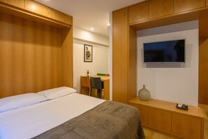 Ein Hotelzimmer mit einem Bett, einem Schreibtisch, einem Sessel, einem Fernseher und einer Vase.