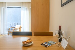 A hotel room with a wooden table, a bottle of wine, two wine glasses, a plate with pastries, and a magazine on the table.