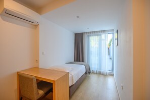 A hotel room with a single bed, a wooden desk, a chair, and a window with curtains.
