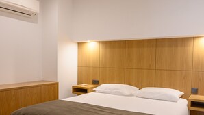 A modern bedroom with a wooden headboard, a large bed with a grey bedspread, a bedside table with a lamp, and a wall-mounted air conditioning unit. - Northern Star - Apartment 2.0 Porto (in the city center) (Porto)