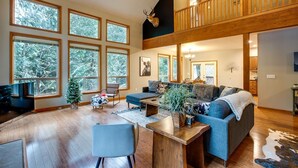 Un salón espacioso con techo alto, ventanas amplias, una zona de estar acogedora y una escalera de madera.