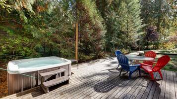 A hot tub on a wooden deck surrounded by trees, with a table and chairs.