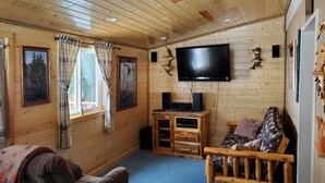 Ein Holzblockhaus-Innenraum mit an der Wand montiertem Fernseher, einer hölzernen Bank und einem Sofa.